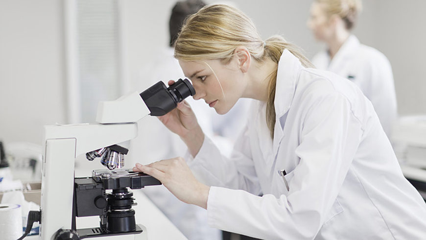 Female scientist looking through a microscope in pathology lab